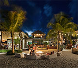 CocoMaya restaurant in Virgin Gorda at night with people sitting around a fire pit on the sand between tropical trees.