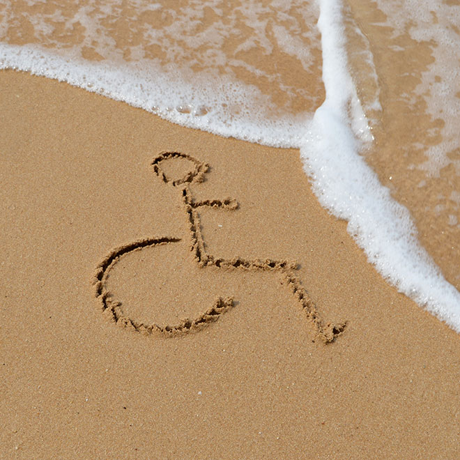 The International Symbol of Accessibility (ISA) draw in the sand with  the water and foam from the ocean washing up on the beach to its right.