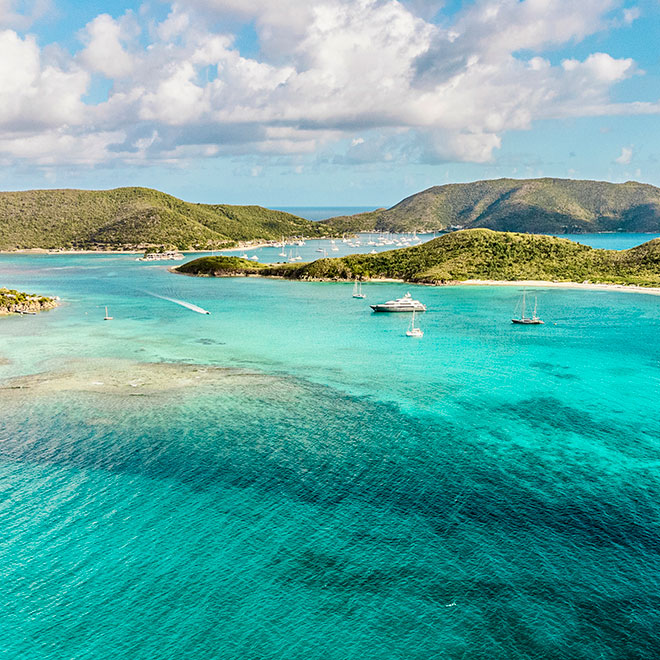 An expansive harbor in Virgin Gorda dotted with boats and surrounded by the green hills of the island and the blue waters of the Caribbean Sea.