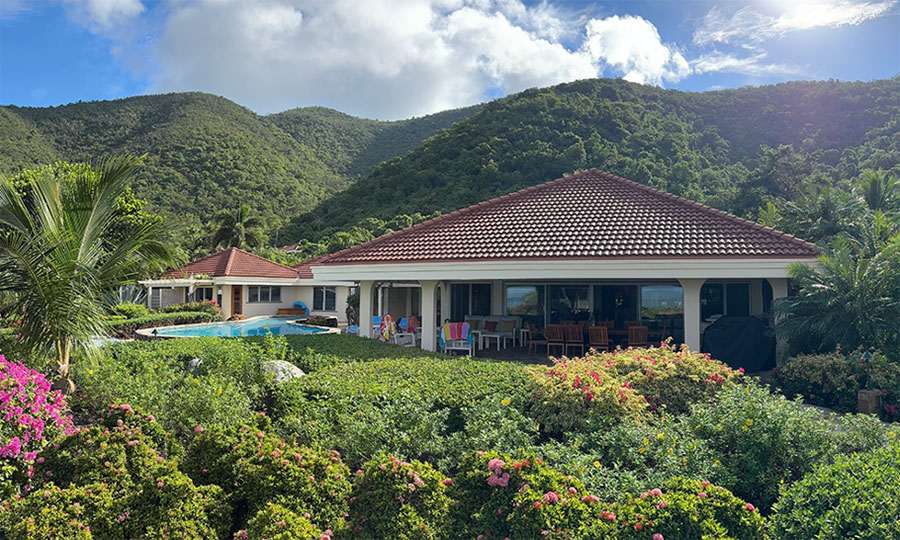 A tropical garden surrounding Beachcomber Villa with the lush green hills and a blue sky with puffy white clouds in the distance.