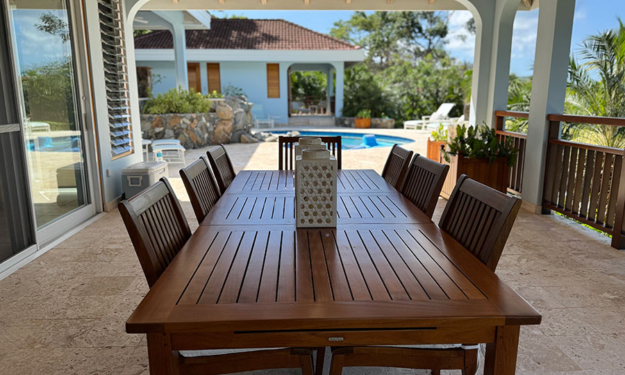Blue Lagoon villa wooden outdoor dining table and chairs with a sundeck with swimming pool in the background.